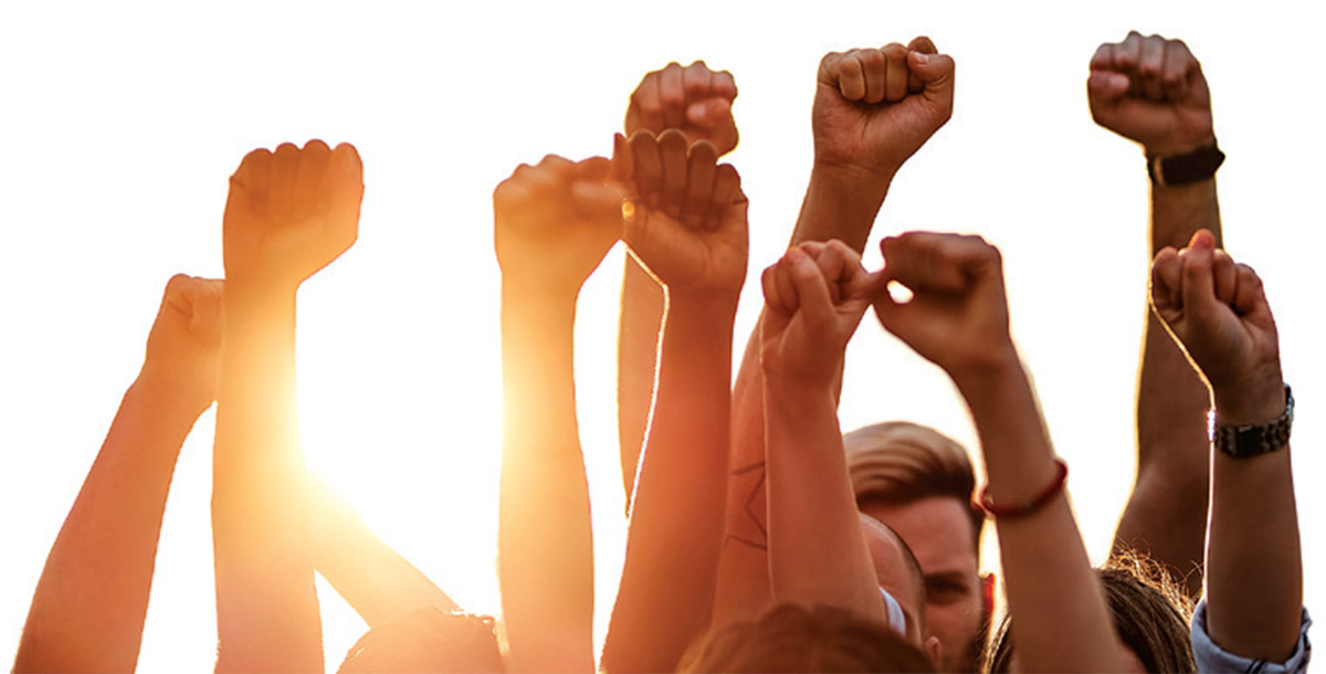 People pump their fists in the air in front of a bright sun.