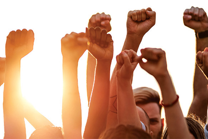 People pump their fists in the air in front of a bright sun.