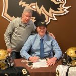 Coach Brian Dobie and recruit Keenan Karish smile while Karish signs with the Bisons