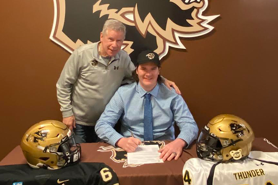 Coach Brian Dobie and recruit Keenan Karish smile while Karish signs with the Bisons