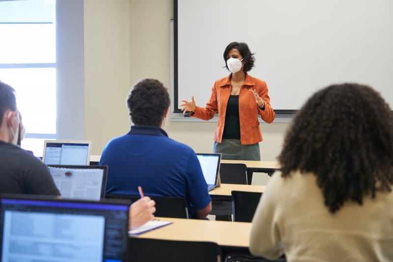 Instructor in KN95 mask at the front of a classroom full of students with backs to camera