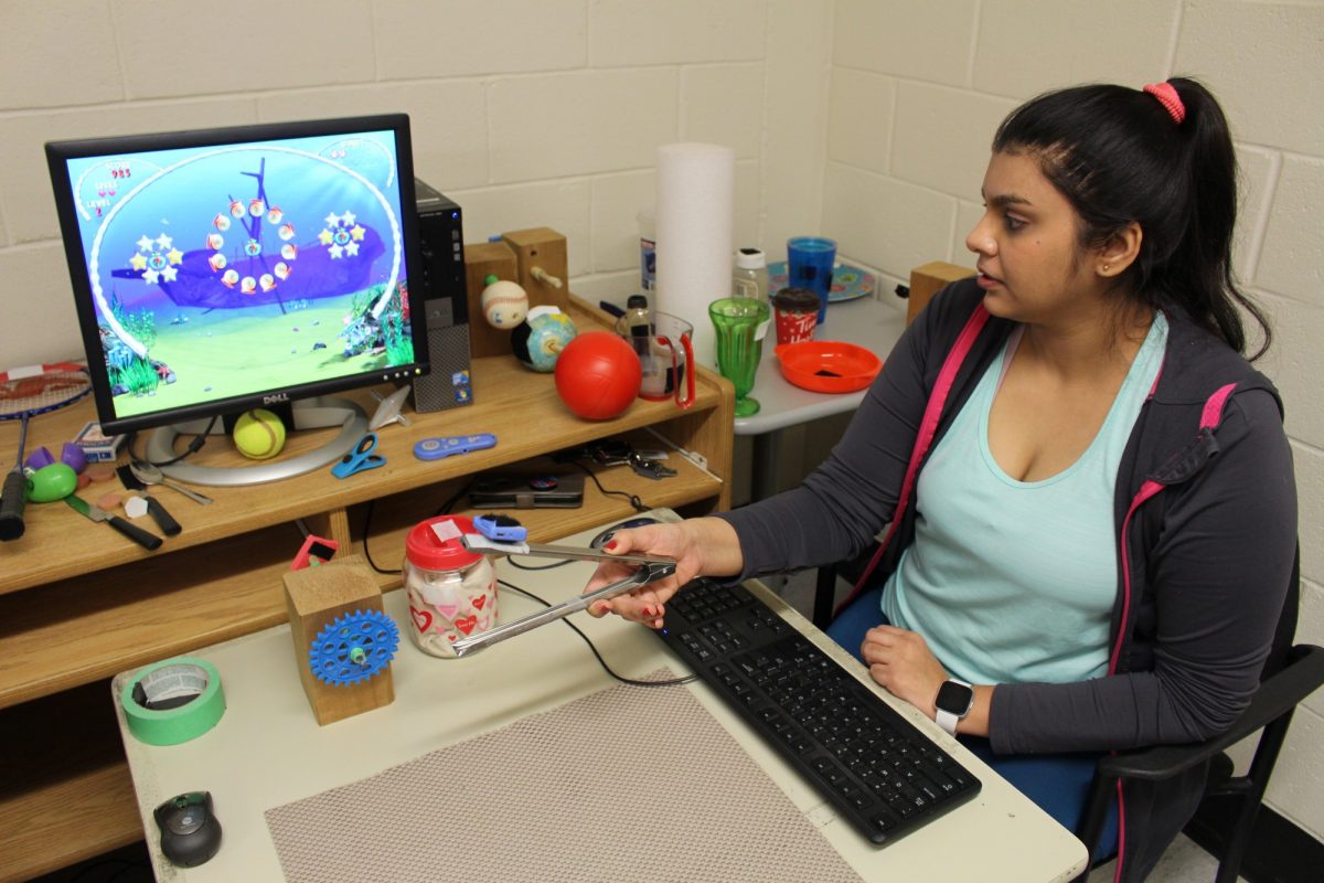 A student sits at a computer using tongs that have a wireless mouse attached.