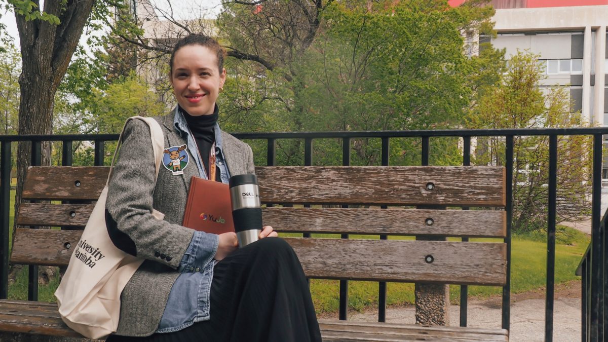 Lori Isber outside on a bench with tote bag, notebook and coffee mug.