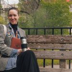 Lori Isber outside on a bench with tote bag, notebook and coffee mug.