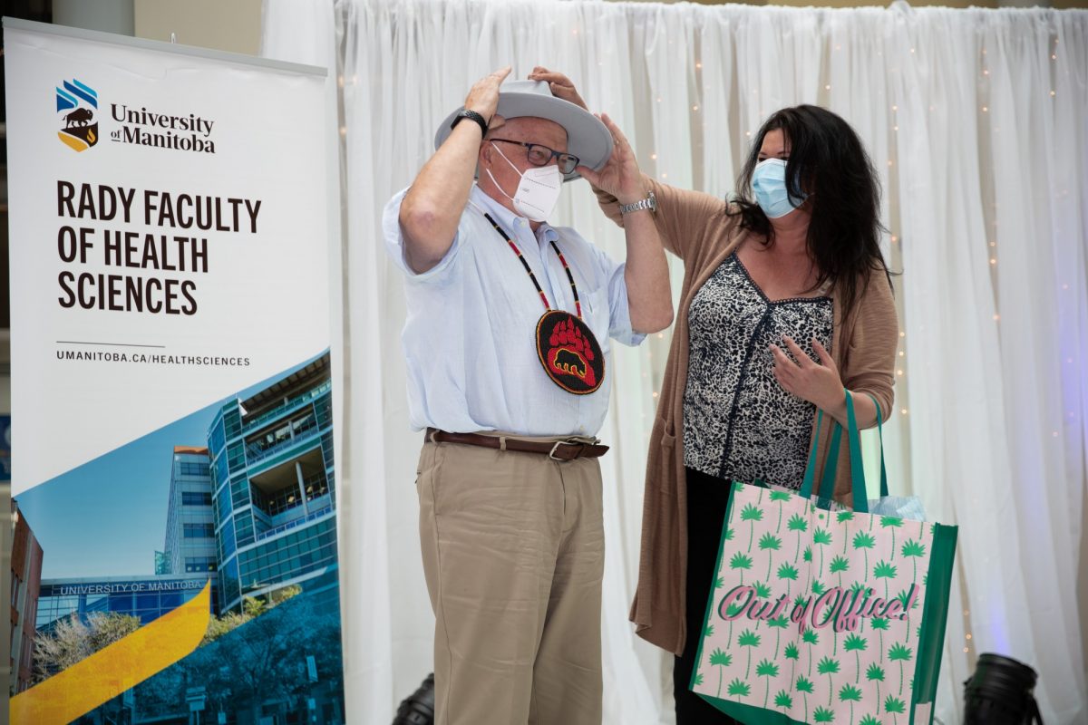 Dr. Brian Postl tries on a hat presented by Melanie MacKinnon on stage at his retirement celebration.