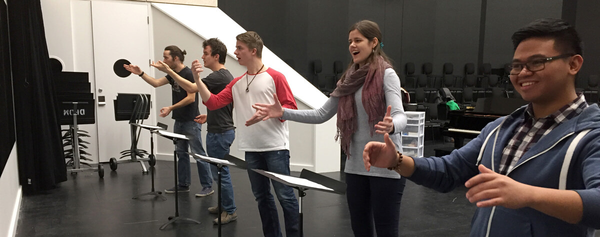 Students in a classroom standing in front of music stands, all engaged at once.