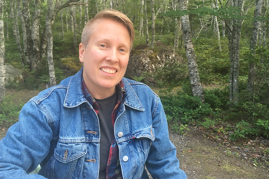 Fenton Litwiller, wearing a jean jacket, smiles in the woods