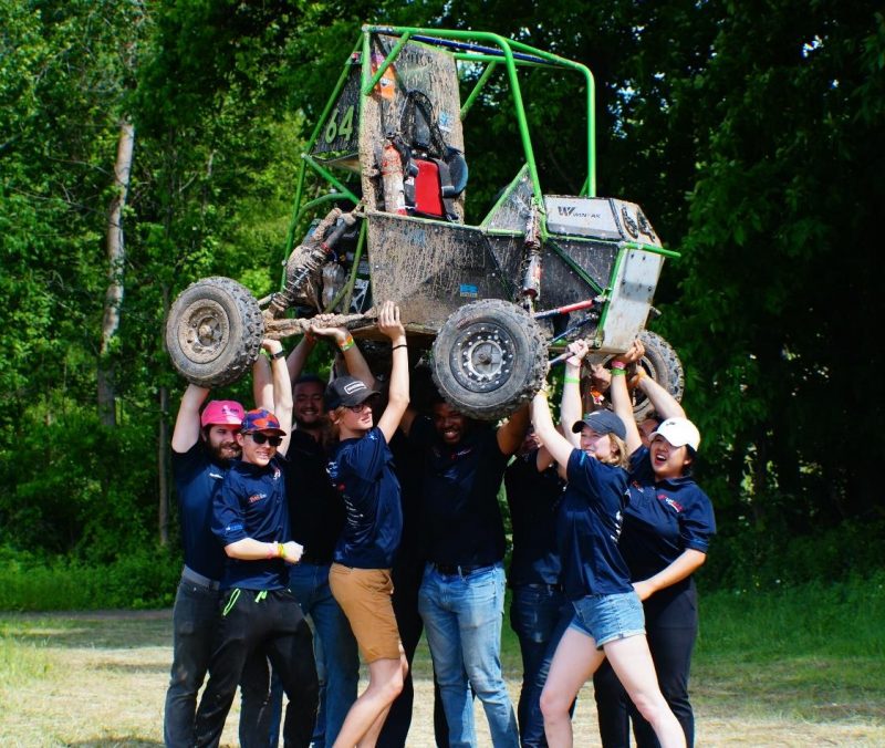 The U M S A E baja team members holding their racing dune buggies over their heads. 