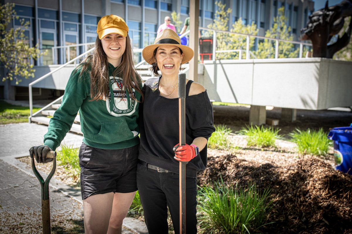 2 smiling people stand together with shovels in hand.