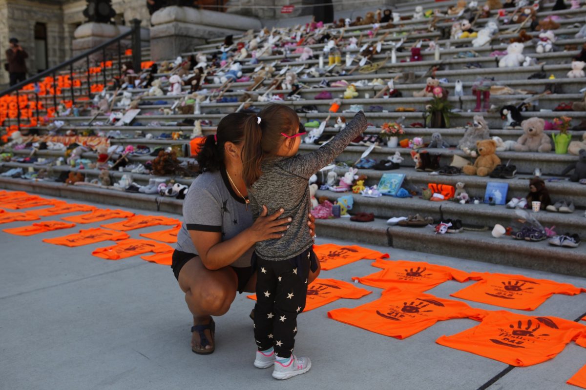 A woman who attended an Indian Day School joins her daughter as they look at the Orange shirts, shoes, flowers and messages on display outside the B.C. legislature in June 2021. THE CANADIAN PRESS/Chad Hipolito