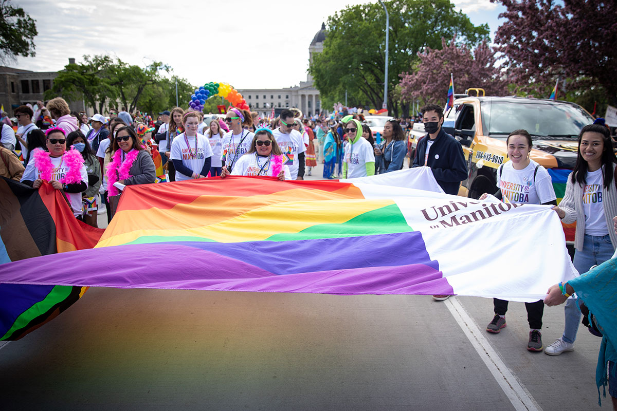 People hold a large UM Pride flag on Memorial Avenue in Winnipeg. Photo from the Winnipeg Pride Parade 2022.