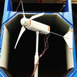 A scale size wind turbine standing in front of the testing tunnel. 