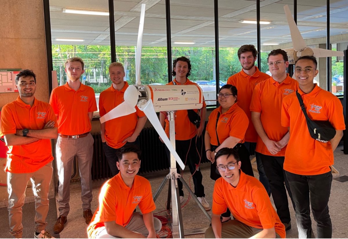 The WE Design team of ten engineering students, each wearing orange shirts and standing alongside their wind turbine.
