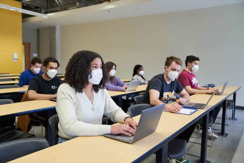 Students wearing KN95 masks and taking notes on laptops and with pencil and paper in a classroom. // Photo from David Lipnowski