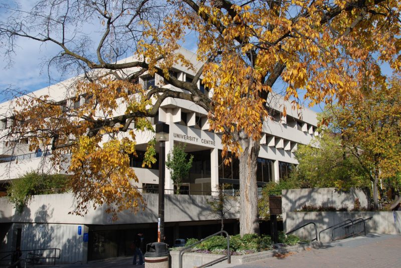 UMSU University Centre in the fall. The leaves on the trees in front of the building have turned a yellow-orange and some have already fallen.