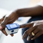A pulse oximeter is places on the finger of a Black person