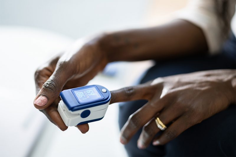 A pulse oximeter is places on the finger of a Black person