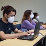 Students wearing KN95 masks type on laptops in a classroom. // Photo from David Lipnowski