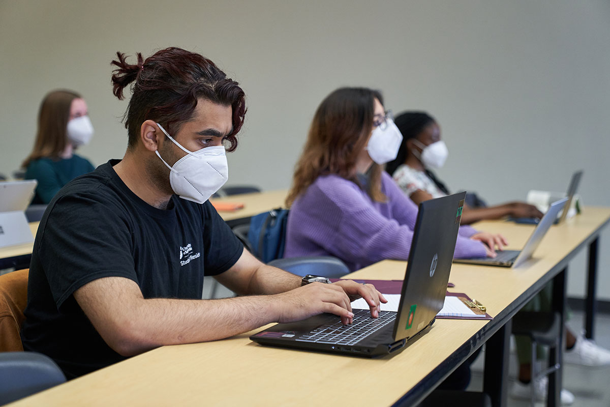 Students wearing KN95 masks type on laptops in a classroom. // Photo from David Lipnowski