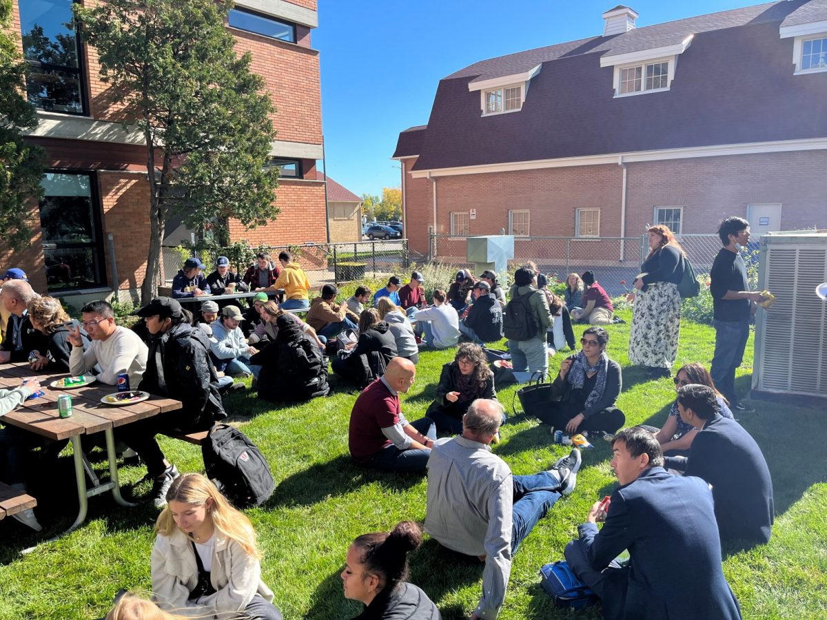 Faculty of Agricultural and Food Sciences students and staff chat at a barbecue in a green space.