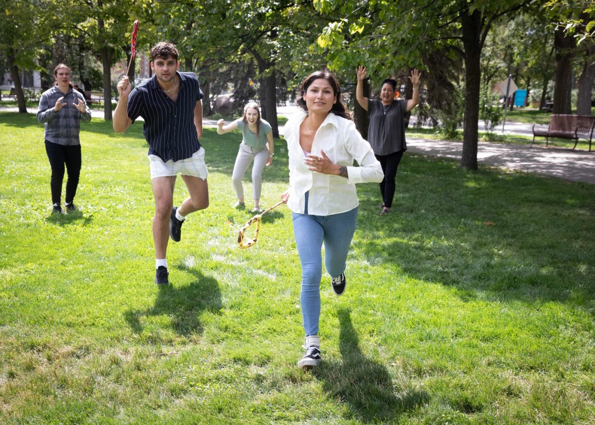 two students running forward with sticks in hand while three people cheer in the background.