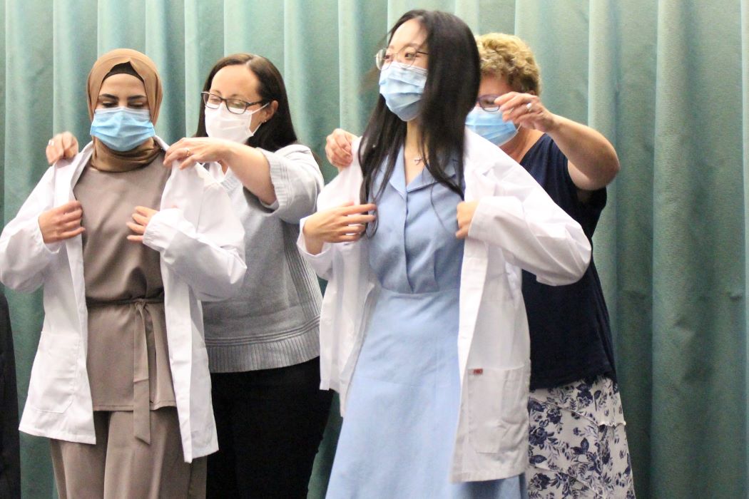 Faculty members help two dental hygiene students to don white coats at Opening Assembly.