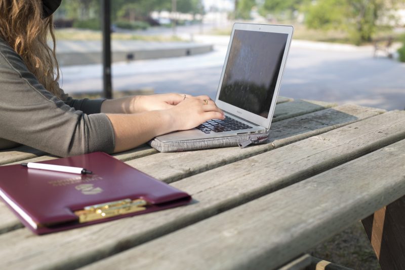 A student works on a laptop at a picnic table.