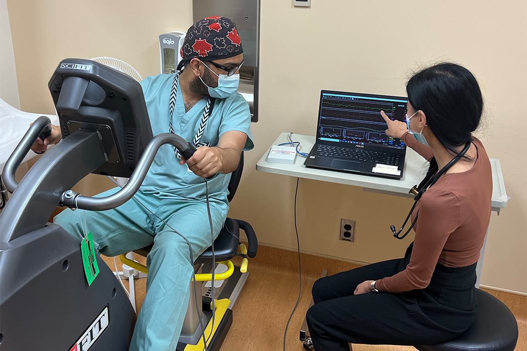 Emelissa Valcourt points to a graph on a laptop screen while Zahurul Islam sits on a stationary bike.