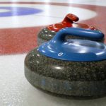 Two curling rocks on ice, one rock has a blue handle, the other is red.