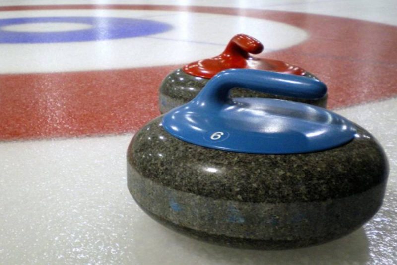 Two curling rocks on ice, one rock has a blue handle, the other is red.