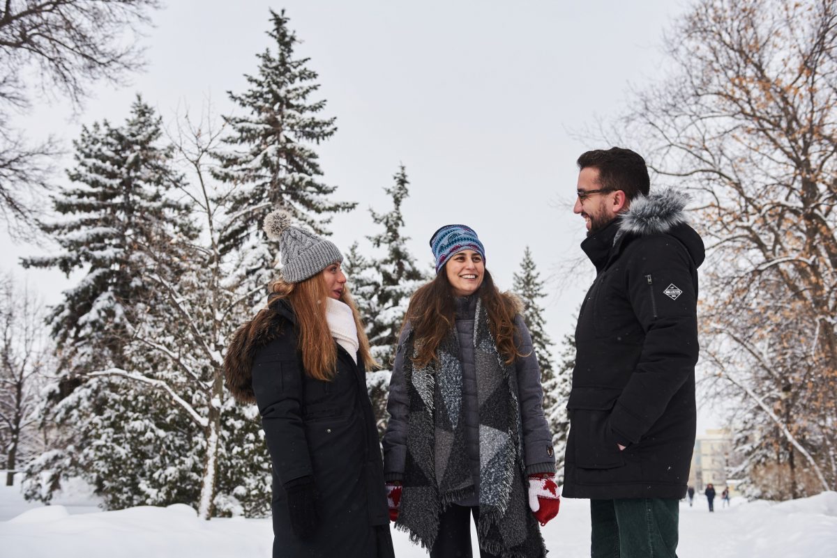 Three students outside in winter with trees in the background.