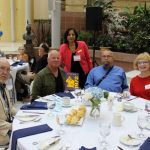 Dr. Lalitha Raman-Wilms, dean of the College of Pharmacy, stands behind alumni from the Pharmacy Class of 1972, who are seated at a table at the Homecoming Breakfast.