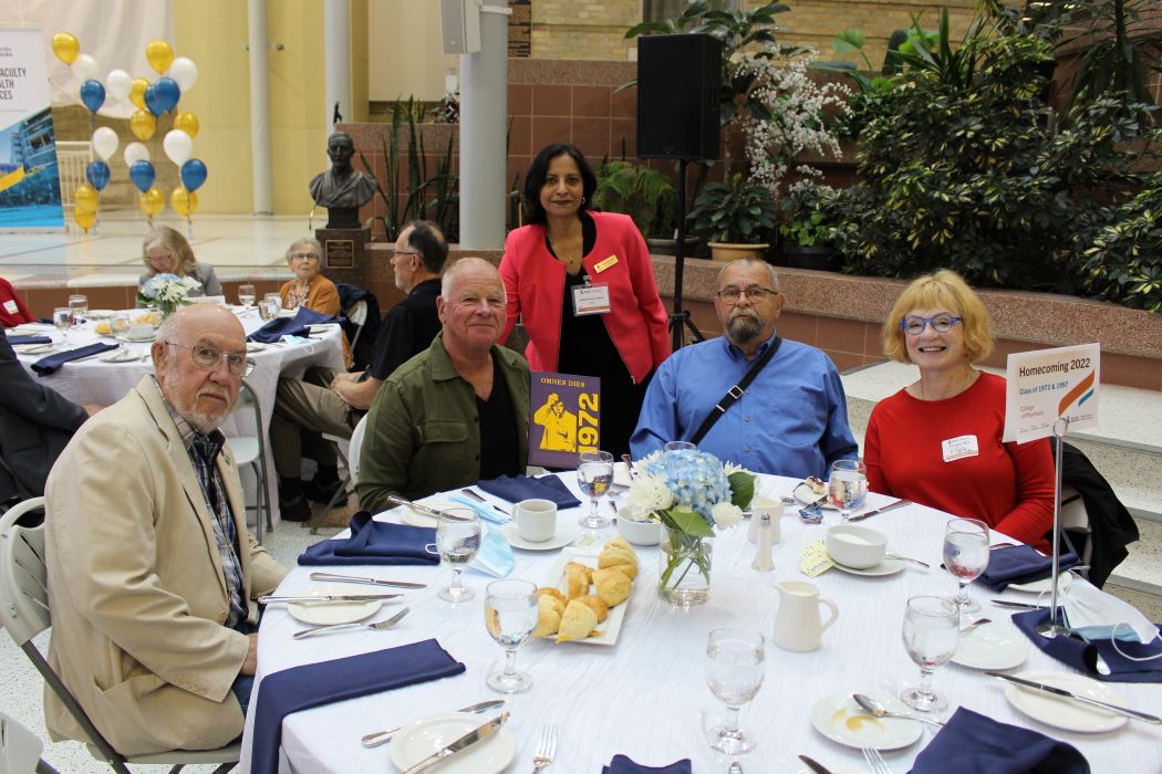 Dr. Lalitha Raman-Wilms, dean of the College of Pharmacy, stands behind alumni from the Pharmacy Class of 1972, who are seated at a table at the Homecoming Breakfast.