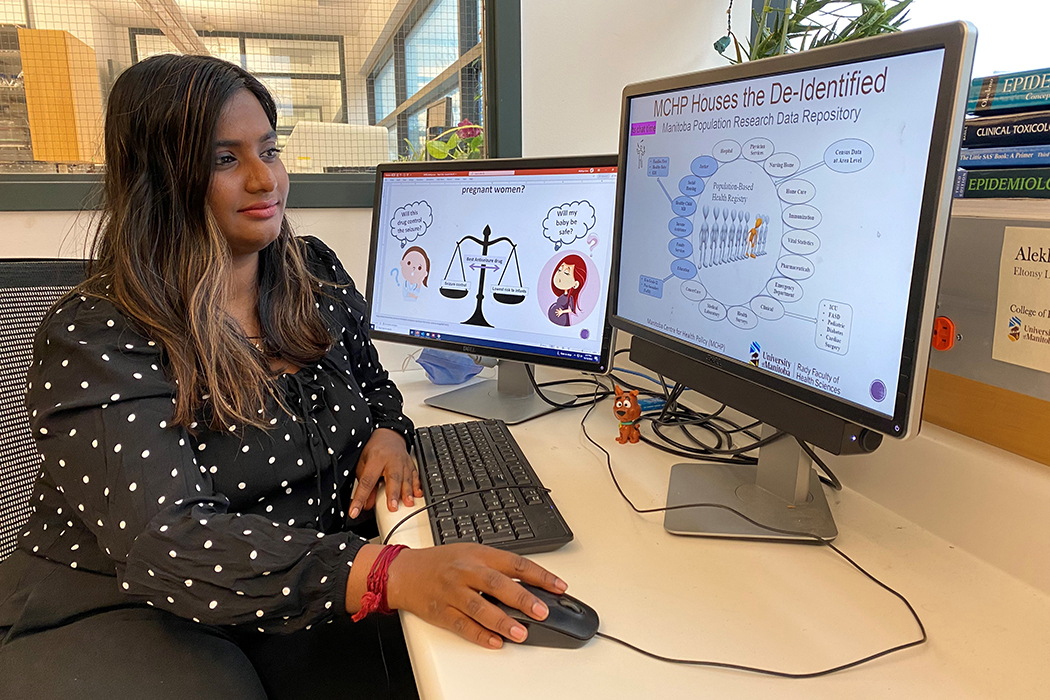 Alekhya Lavu sits at a desk looking at one of two computer monitors.