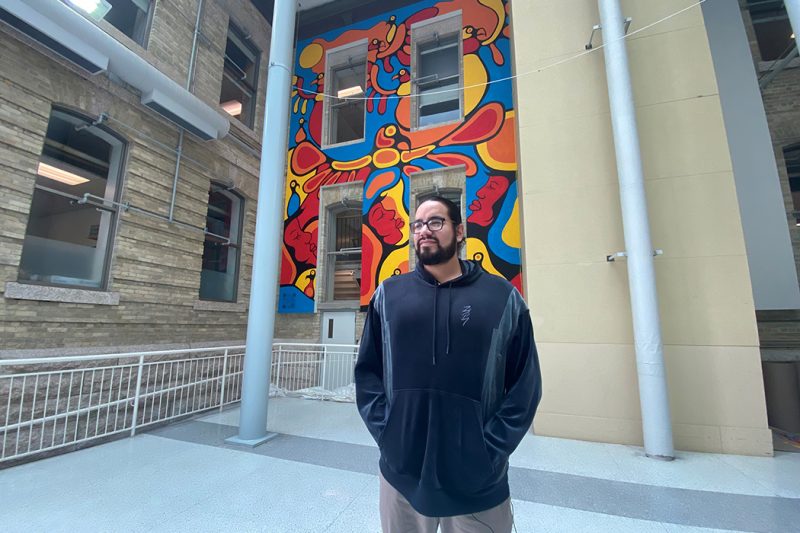 Blake Angeconeb stands in front of the mural he painted.