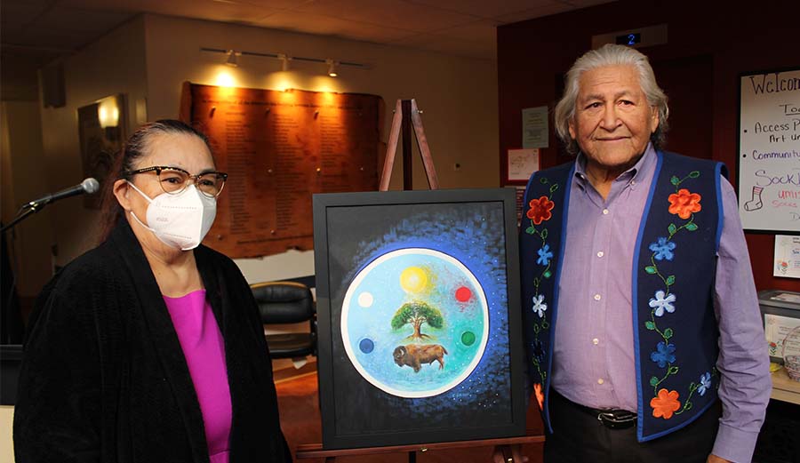 Two people stand beside an easel with art on it.