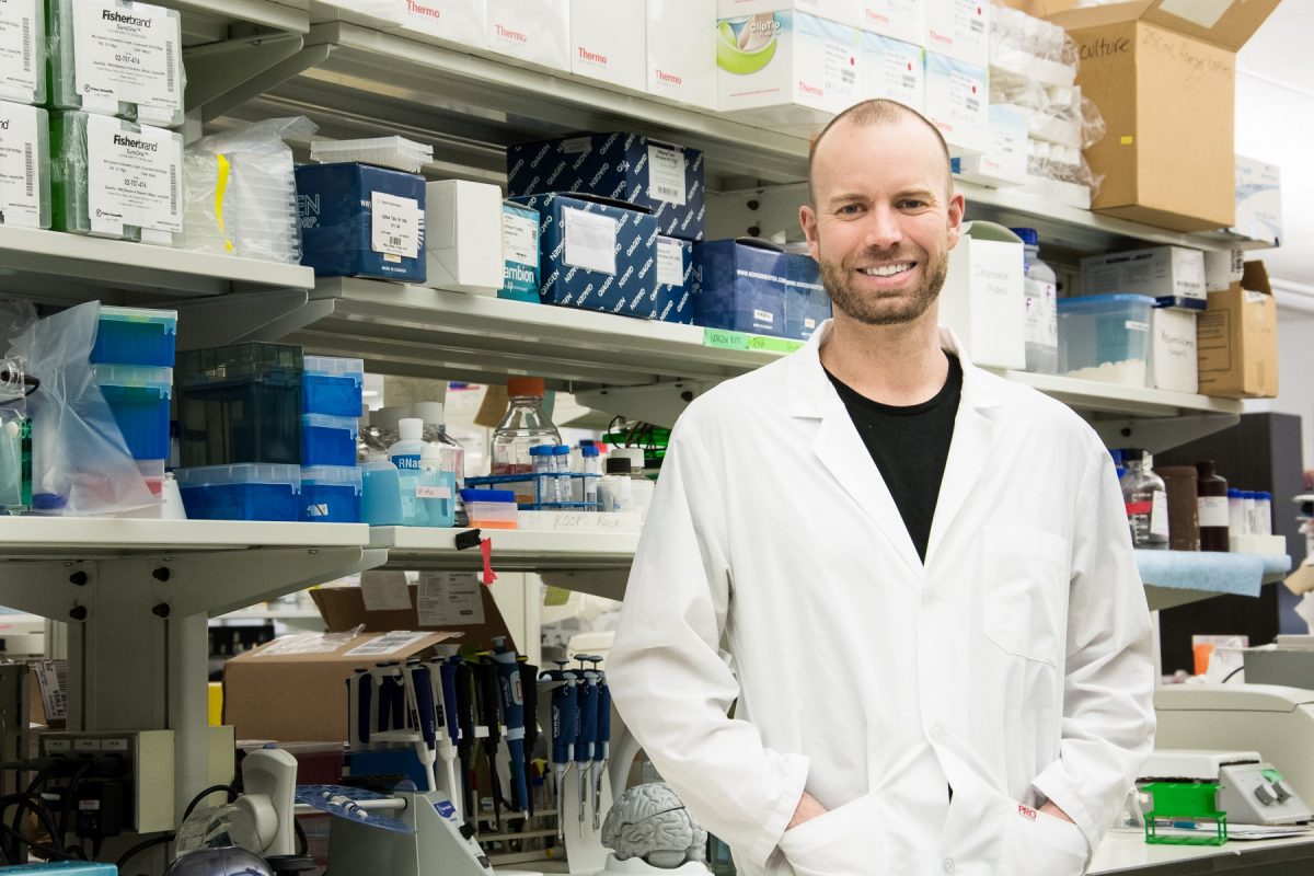 Brent Guppy stands in his lab wearing a white lab coat.