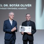 Dr. Ovliver Botar stands on stage with Rector József Fülöp and holds a glass award