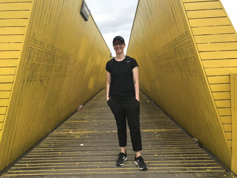 Caucasian student dressed in black stands in front of a yellow bridge