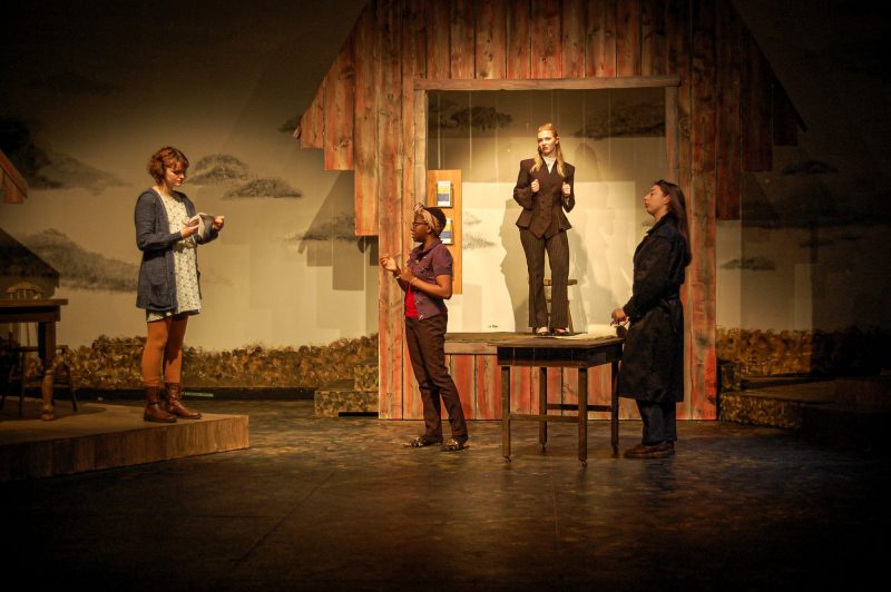 Four actors on stage with farmhouse backdrop.