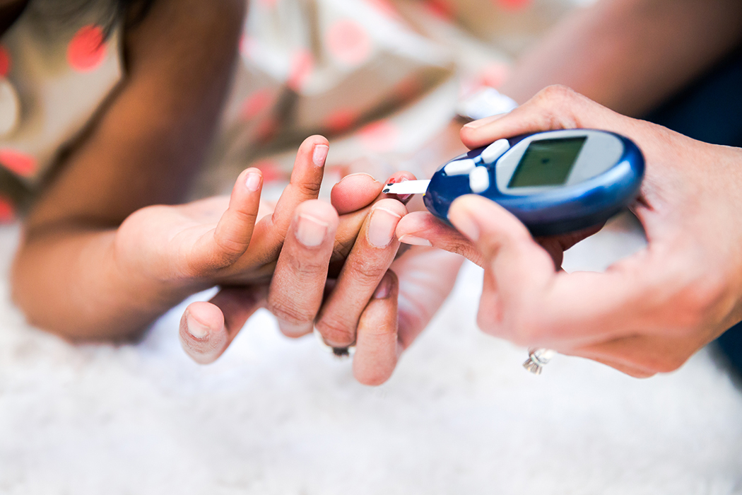 Mother is holding her daughter's hand and is checking her child's diabetes by monitoring blood glucose with a device.