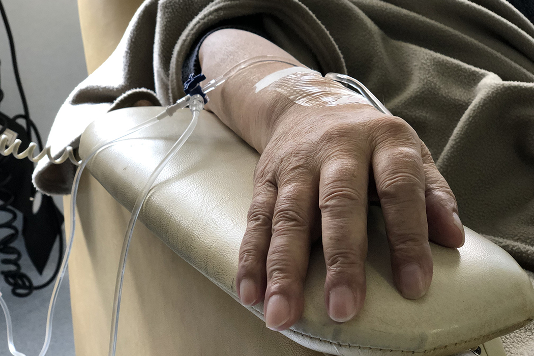 A man's arm on an armrest is attached to an IV with tubes.