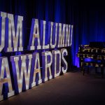 View of a stage with large letters that speel out UM Alumni Awards with a grand piano in the background.