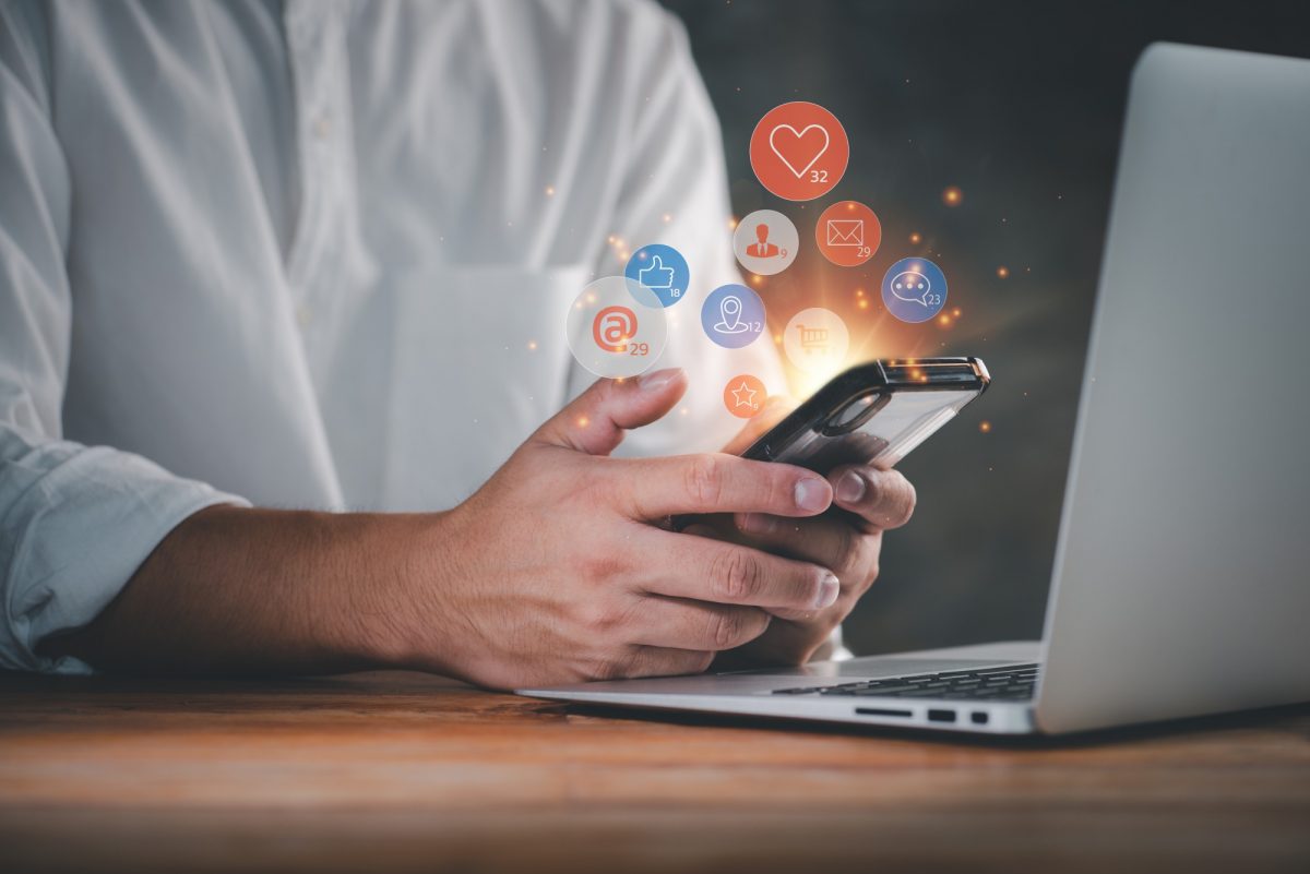 Person at a computer holding a phone with social media icons popping out.