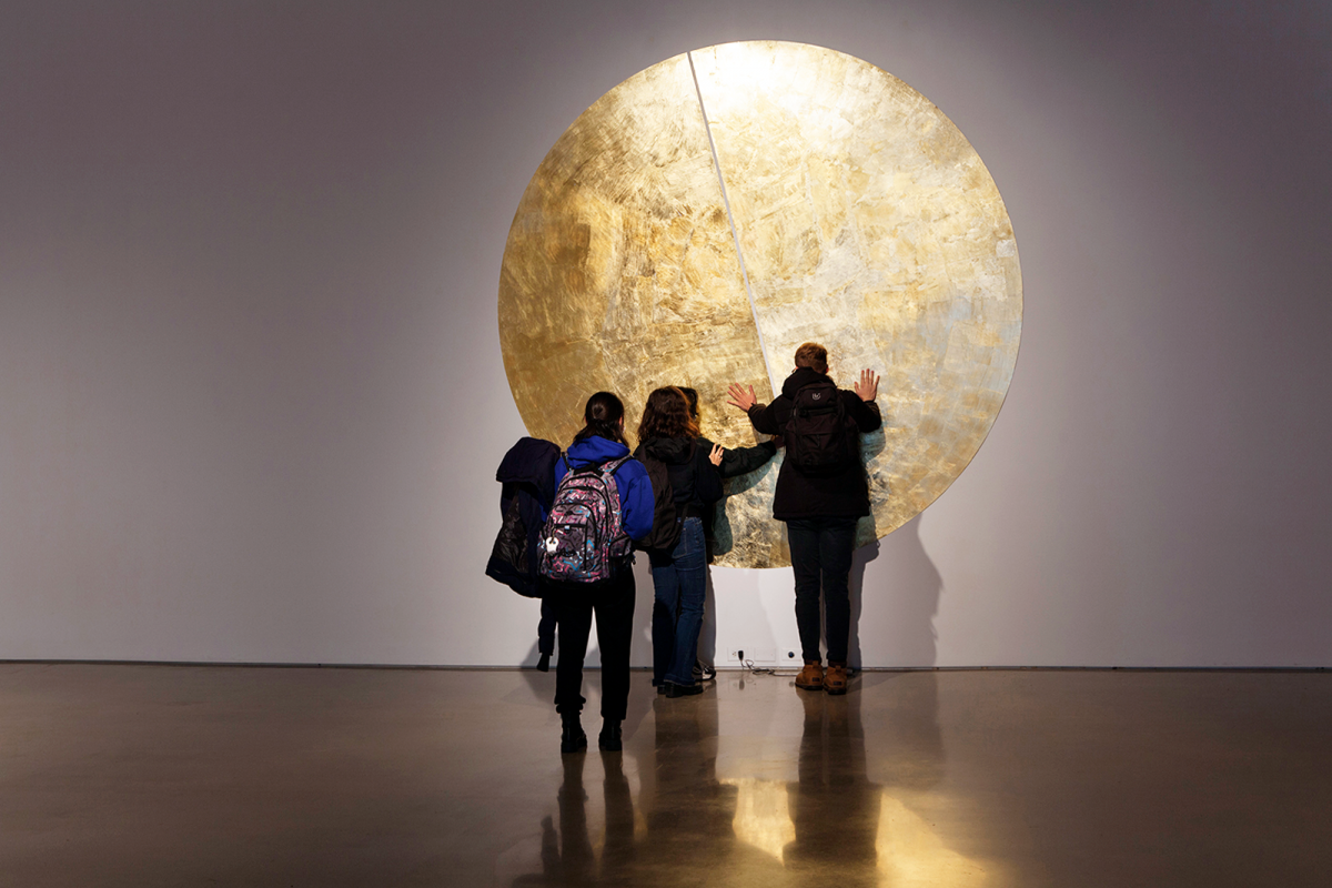 People standing in front of circular gold leaf artwork.