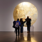 People standing in front of circular gold leaf artwork.