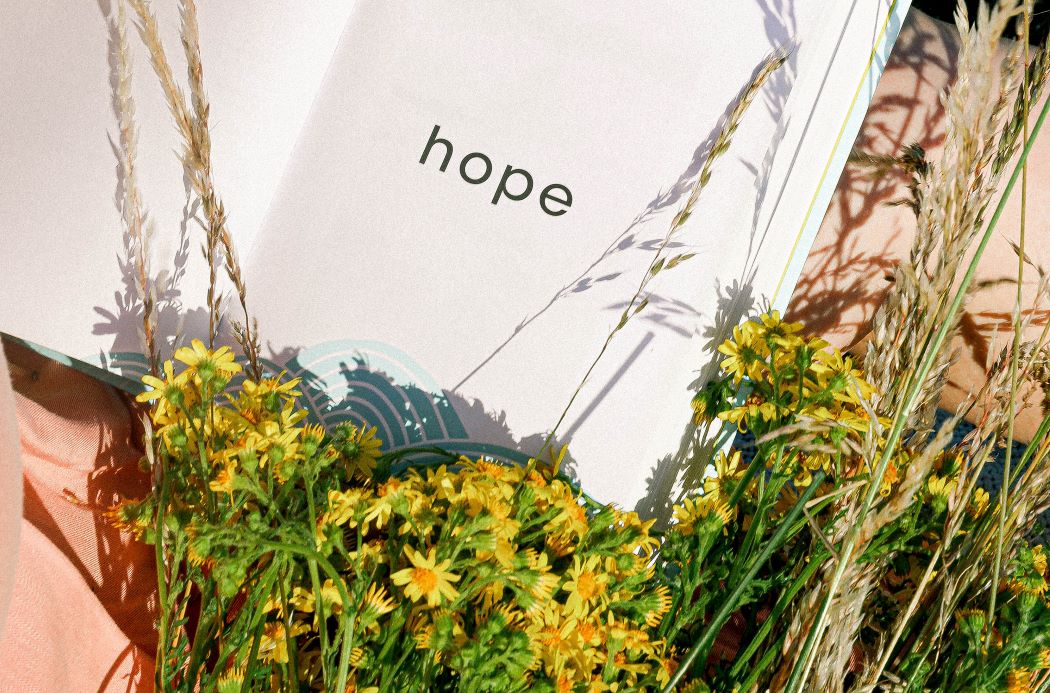 Yellow flowers are clustered around an open card that says "hope."