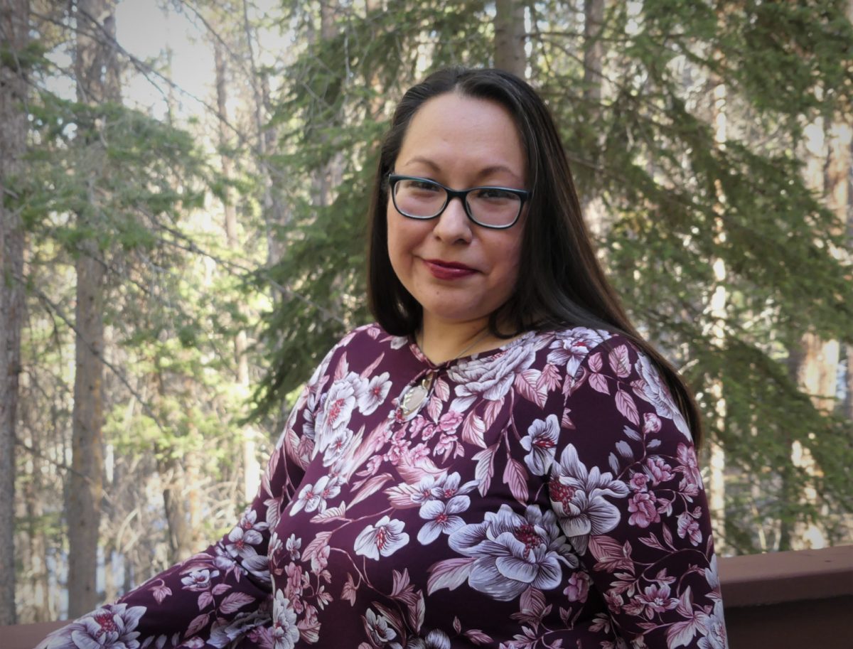 Janine Windolph in flowered blouse in front of a forest of pine trees.