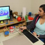 Dr. Anuprita Kanitkar holds a pair of tongs with a sensor attached while looking at a computer game on a monitor.