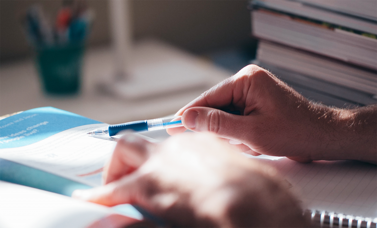 Person reading textbook with pen in hand